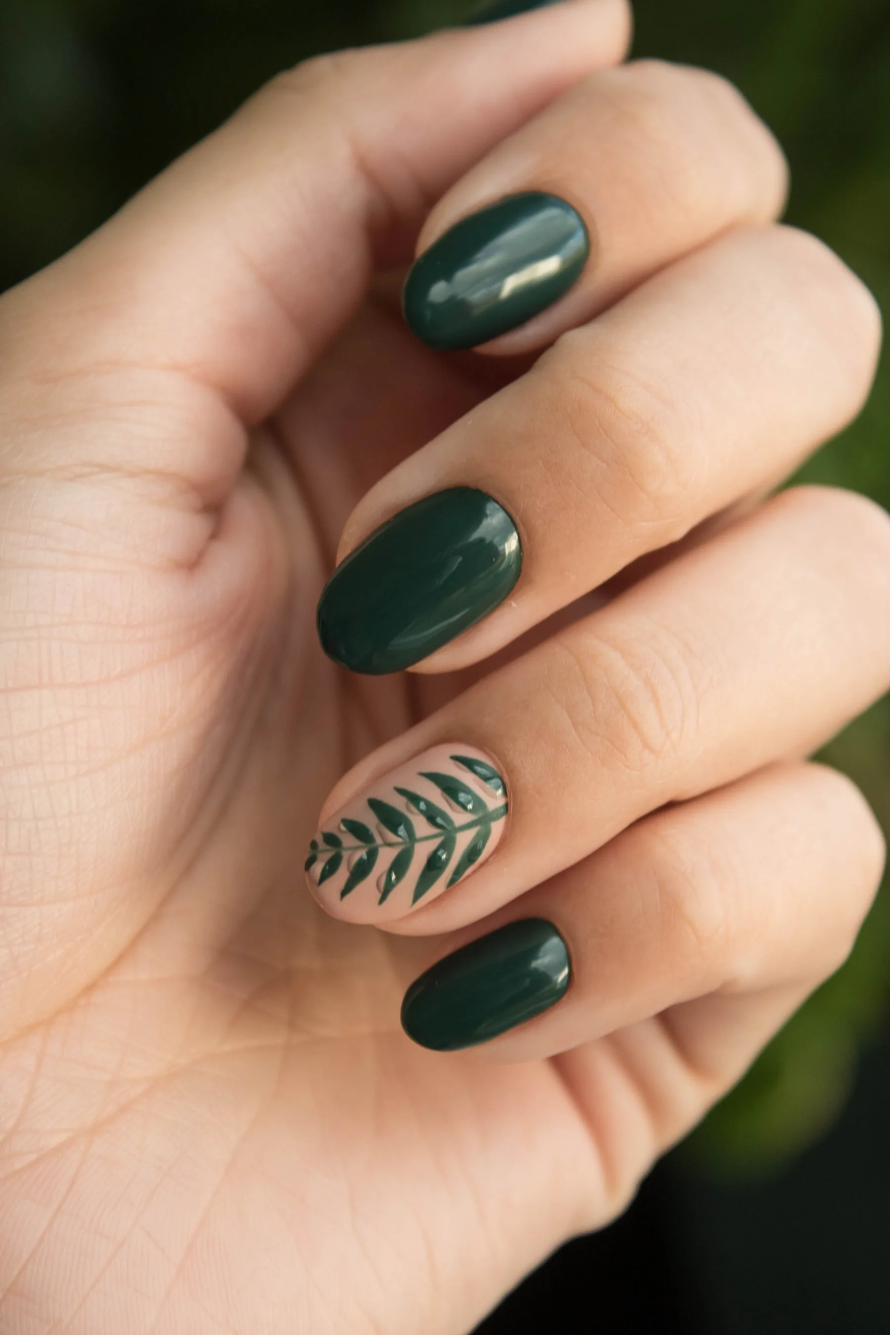 Mano con uñas cortas en verde oscuro y un detalle botánico